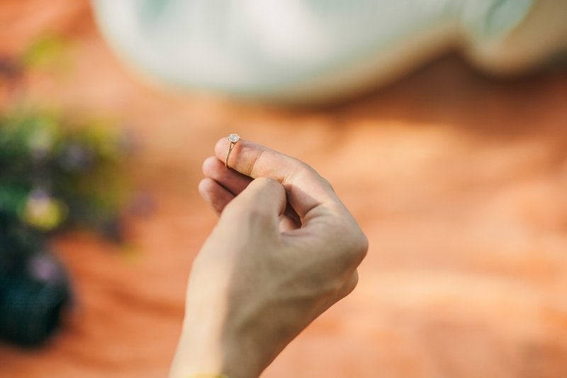 žena drží na prste zlatý diamantový zásnubný prsteň