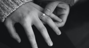 mužská ruka drží ženskú ruku so zásnubným prsteňom na prstenníku na čiernobielom pozadí